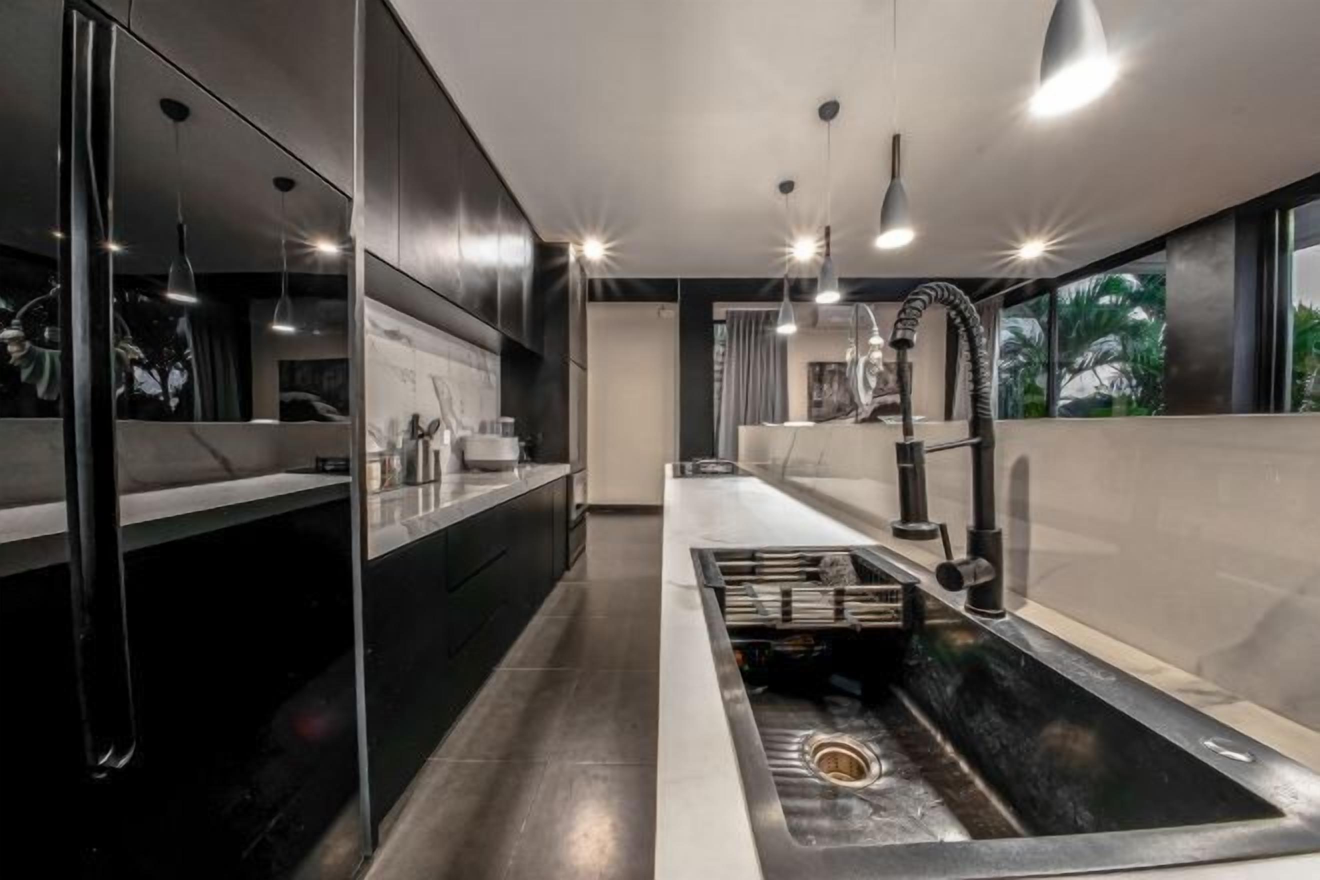 A modern bathroom with a central sink, a mirror, and a window providing a view of palm trees.