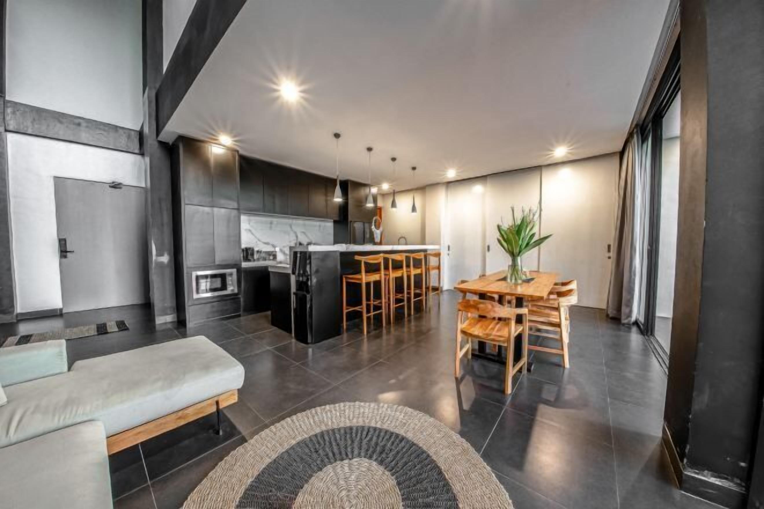 A modern kitchen with dark tiles, a dining area with wooden furniture, and a large window.