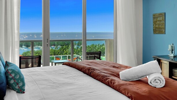 Habitación de hotel con un ventanal que ofrece vistas al mar y a barcos.