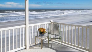A wooden deck with a white railing overlooking a beach with waves. - High Tide Paradise (St. Augustine)