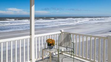 A wooden deck with a white railing overlooking a beach with waves.