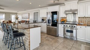 A spacious kitchen with white cabinets, a stainless steel refrigerator, a gas stove, and a large island with bar stools. - High Tide Paradise (St. Augustine)