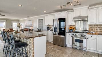 A spacious kitchen with white cabinets, a stainless steel refrigerator, a gas stove, and a large island with bar stools.