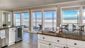 A kitchen with large windows overlooking the beach, a dining area with chairs, and a kitchen island.