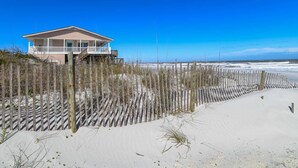 A beachfront house with a balcony overlooking the ocean, surrounded by a wooden fence and sand dunes. - High Tide Paradise (St. Augustine)