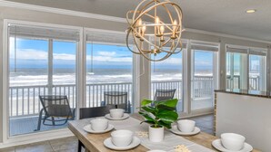 A dining area with a view of the ocean, a chandelier, and a table set with white dishes and a potted plant. - High Tide Paradise (St. Augustine)