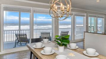 A dining area with a view of the ocean, a chandelier, and a table set with white dishes and a potted plant.