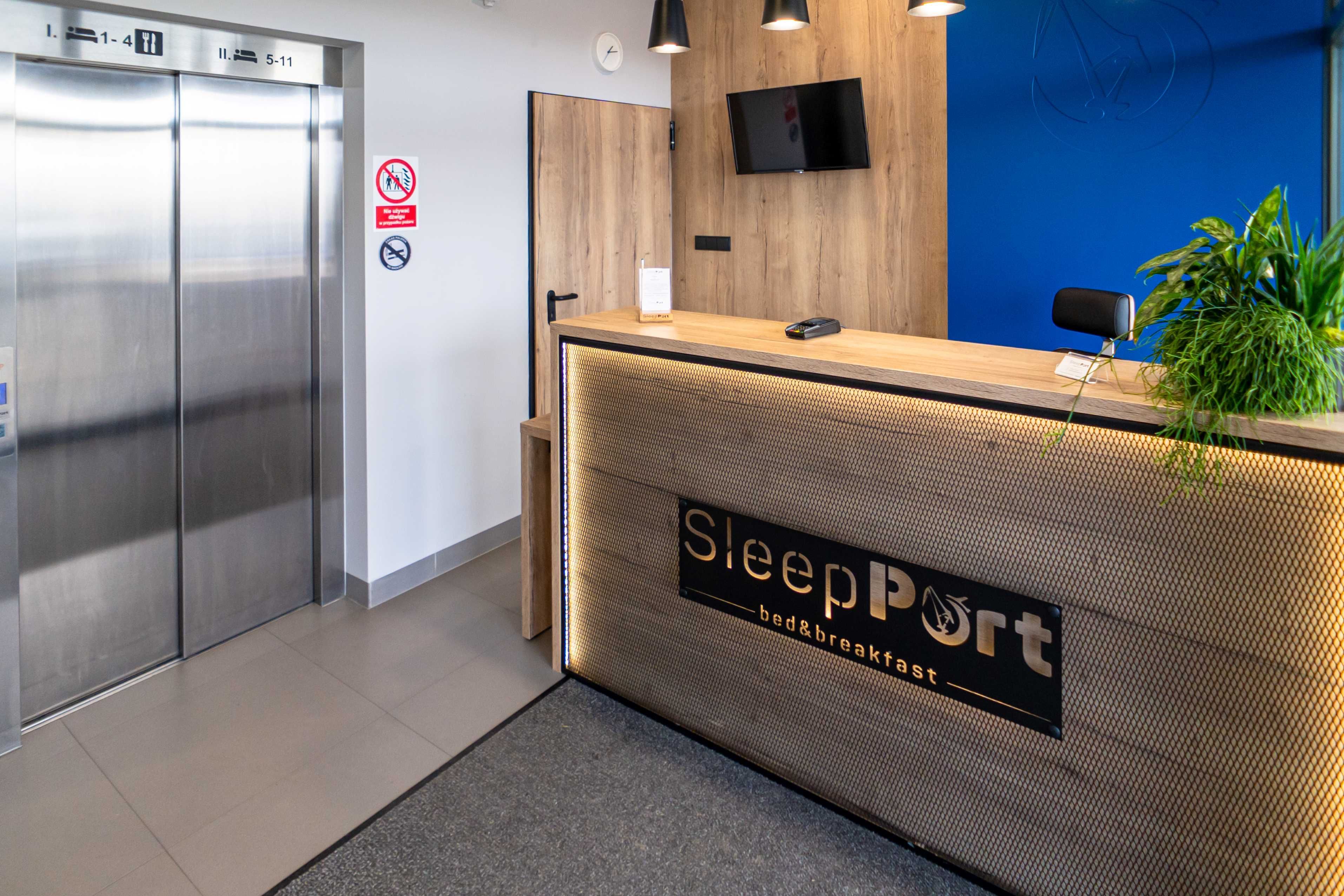 A reception desk with a sign reading "SleepPort bed&breakfast," a mounted television, and a no-smoking sign.