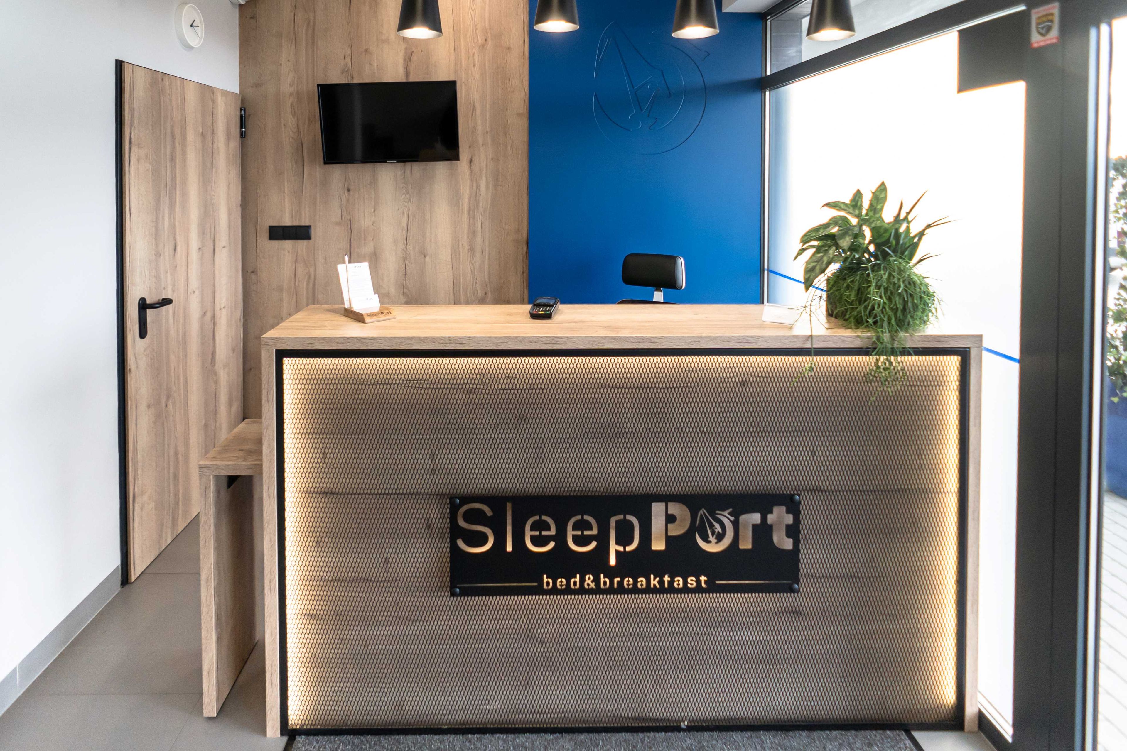 Uma receção com uma placa a indicar "SleepPort bed&breakfast" e uma televisão montada na parede.