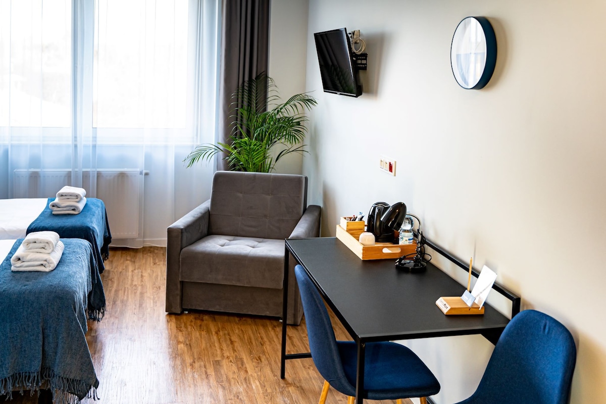 A hotel room with two beds, a sofa, a table with a tray, a TV, and a plant.