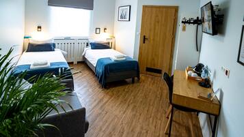 Habitación de hotel con dos camas, un escritorio, una silla, un radiador, una puerta de madera y un televisor fijado a la pared.