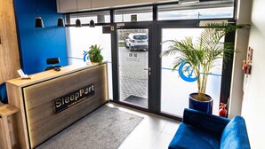 A reception area with a wooden desk, a blue couch, and a potted plant. - Sleep Port (Gdańsk)