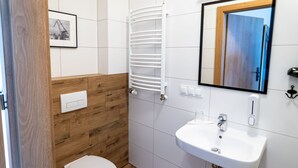 A bathroom with a white sink, wooden panel wall, white toilet, and a towel rack.