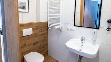 A bathroom with a white sink, wooden panel wall, white toilet, and a towel rack.