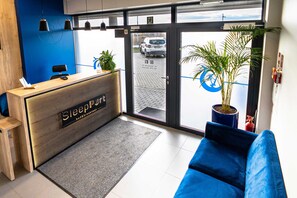 Ett väntrum med en blå soffa, en reception i trä och ett stort fönster med utsikt över gatan.