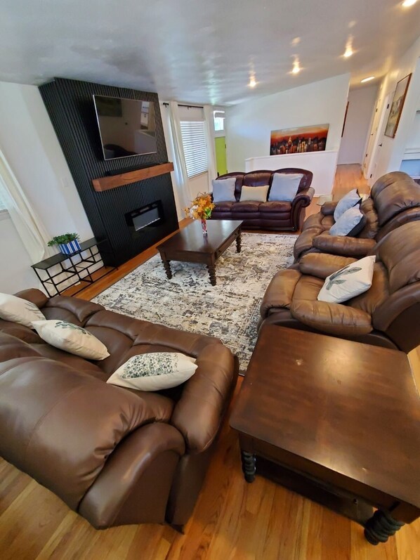 A living room with brown leather sofas, a coffee table, and a flat-screen TV mounted on a black wall.