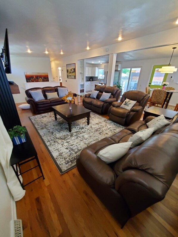 A modern living room with leather sofas, a coffee table, and a rug. There is a kitchen in the background and a dining area with chairs.