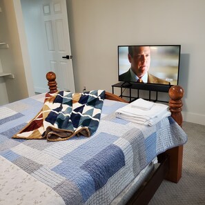 A bed with a patterned blanket, a folded towel, and a television displaying a show.