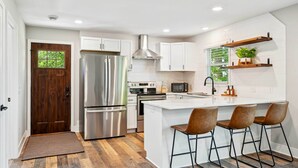Une cuisine moderne avec des meubles blancs, des appareils en acier inoxydable et un îlot central doté de tabourets de bar.