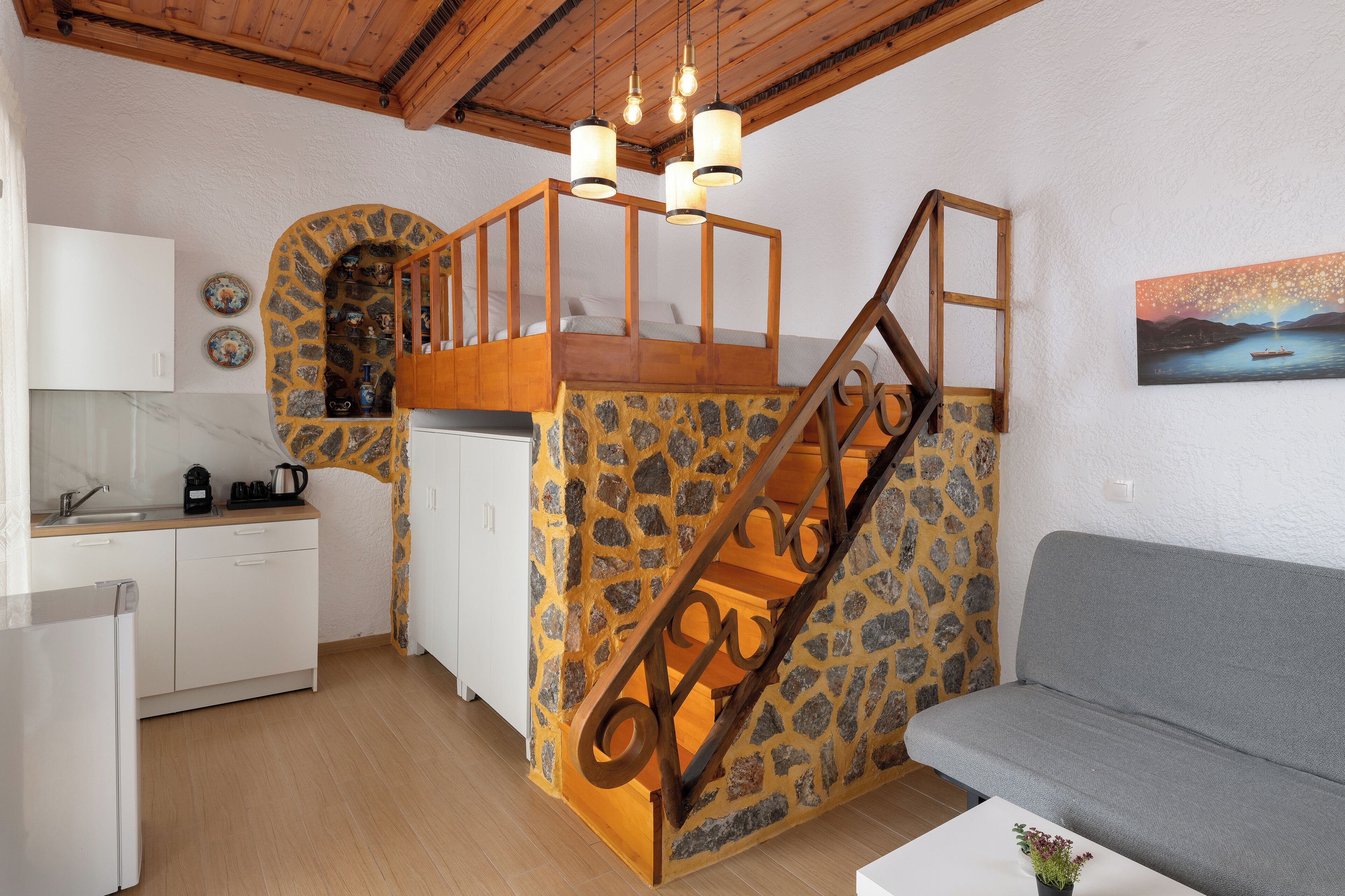 A compact kitchen with a stone accent wall, a wooden staircase, and a grey sofa.