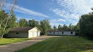 A two-story house with a garage and a covered porch, surrounded by a well-maintained lawn and trees. - Revilo Timber Haven Mauston - Near The Dells and Castle Rock Lake! (Mauston)