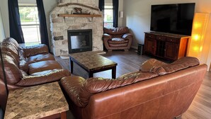 A living room with a stone fireplace, leather sofas, a coffee table, and a flat-screen TV. - Revilo Timber Haven Mauston - Near The Dells and Castle Rock Lake! (Mauston)