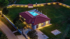 Una casa moderna con piscina, un patio cubierto y un césped bien iluminado.
