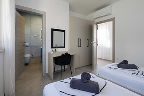 Une chambre d’hôtel moderne, équipée d’un lit, d’un bureau, d’une chaise et d’une salle de bain visible à travers une porte ouverte.