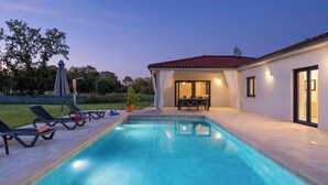 Una piscina con sillones de descanso y un porche cubierto.