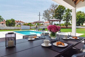 Un espace extérieur aménagé pour les repas, avec une piscine, des parasols et une vue sur le quartier.