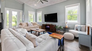 A spacious living room with a ceiling fan, a large flat-screen TV, and a cozy seating area with a sofa and ottoman. - Crescent Cove (St. Augustine)