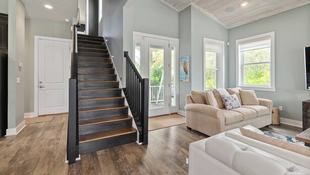 A spacious living room with a staircase, a beige sofa, and a large window providing natural light. - Crescent Cove (St. Augustine)