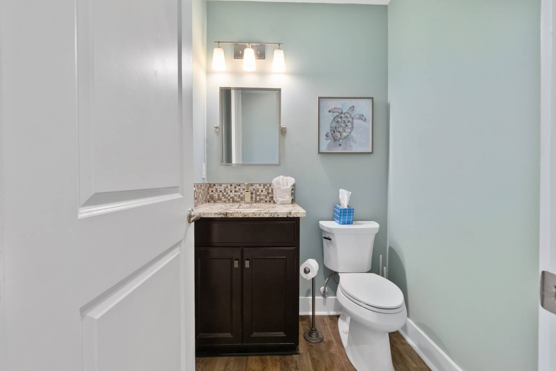A bathroom with a white toilet, dark wooden cabinet, and a light blue wall.