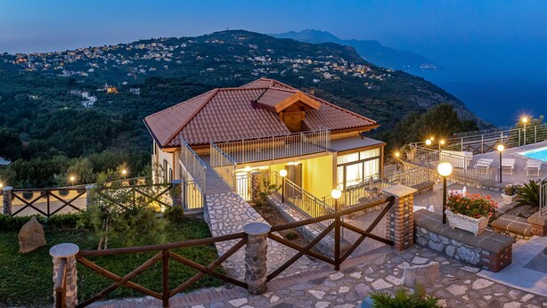 A villa with a swimming pool, stone pathway, and a view of the sea.