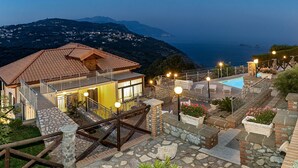 A hillside villa with a swimming pool, stone pathways, and a view of the sea.
