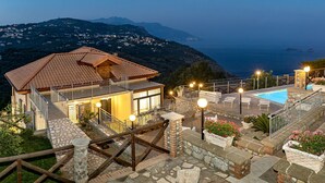A two-story building with a pool, stone steps, and a view of the sea.
