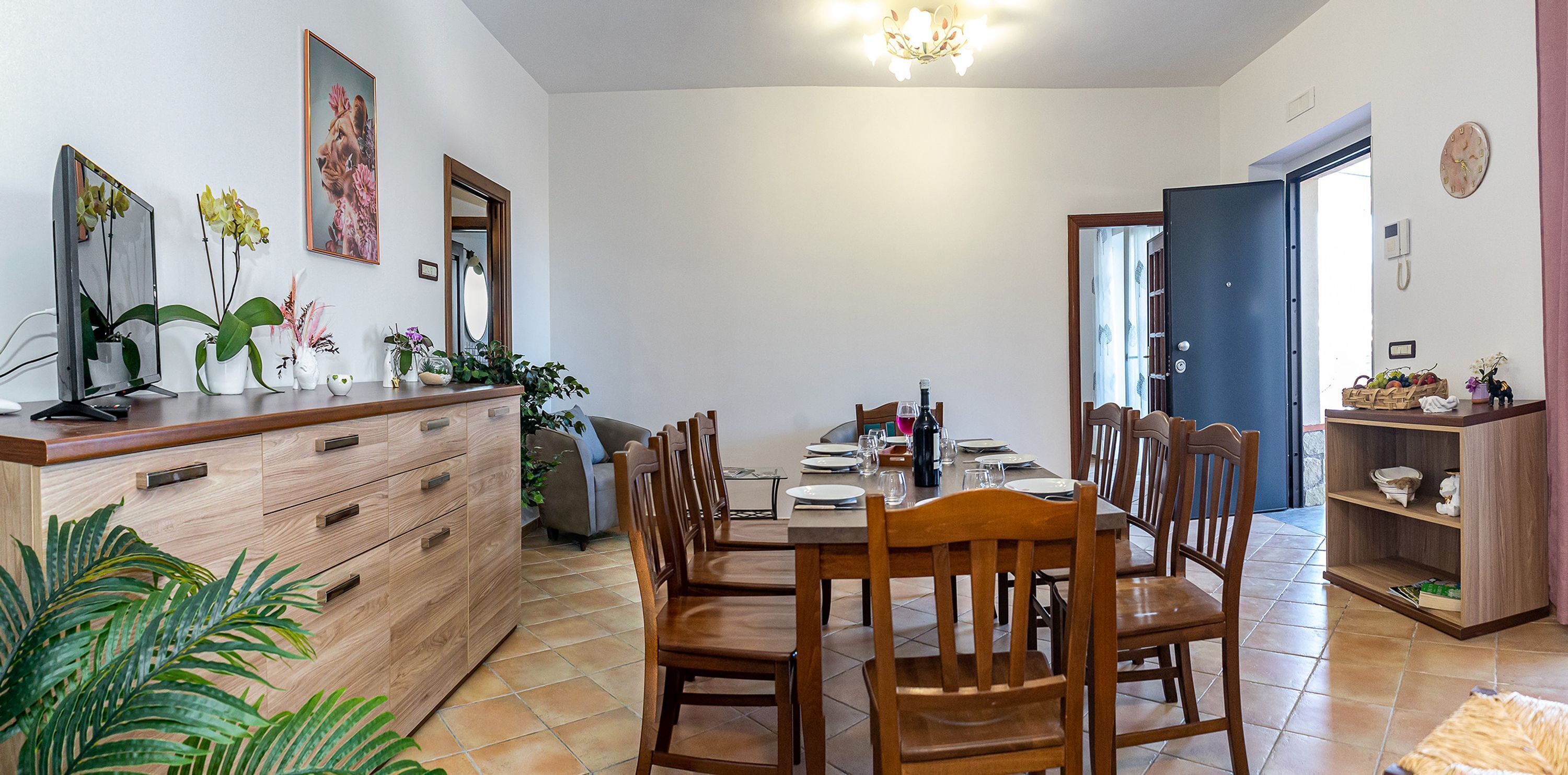 Un comedor con una mesa de madera preparada para cuatro personas, rodeada de sillas de madera. Hay un mueble de madera con cajones y un espejo en la pared.