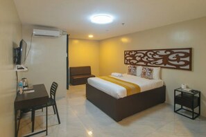 Una habitación de hotel con cama, escritorio, silla, televisor y un elemento decorativo en la pared.