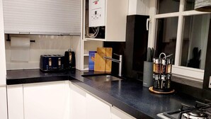 Una cocina moderna con armarios blancos, encimera negra, horno integrado y ventana con persianas.
