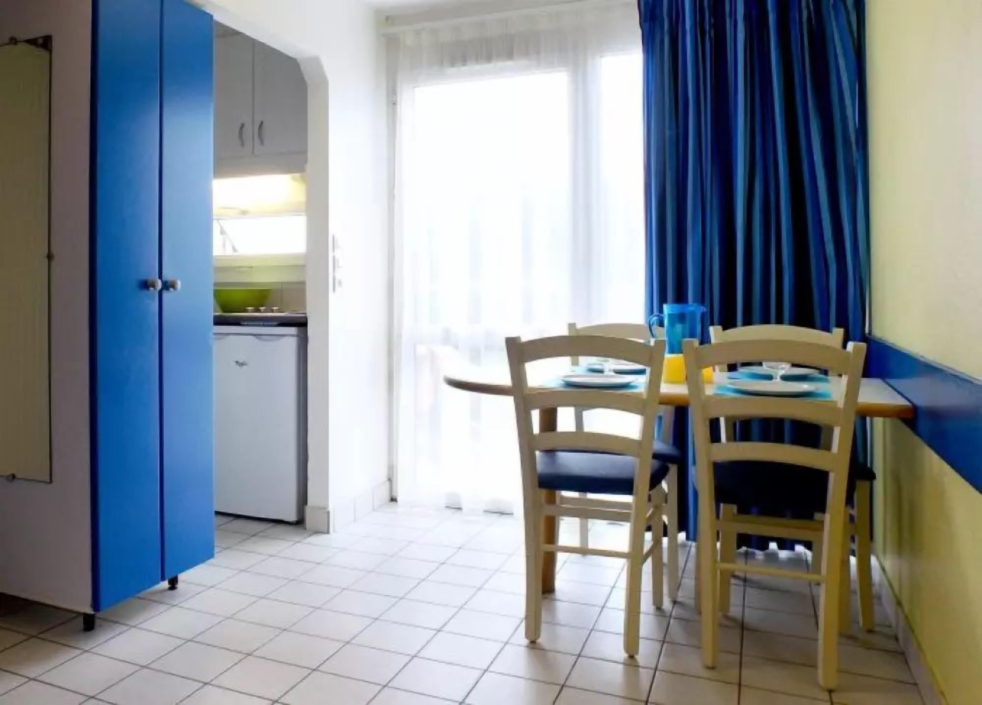 A compact kitchen with a white fridge, a blue cabinet, and a dining area with two wooden chairs and a table.