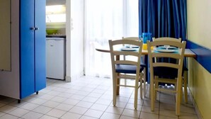 A compact kitchen with a white fridge, a blue cabinet, and a dining area with two wooden chairs and a table. - Vvf Villages Piriac Sur Mer (Piriac-sur-Mer)