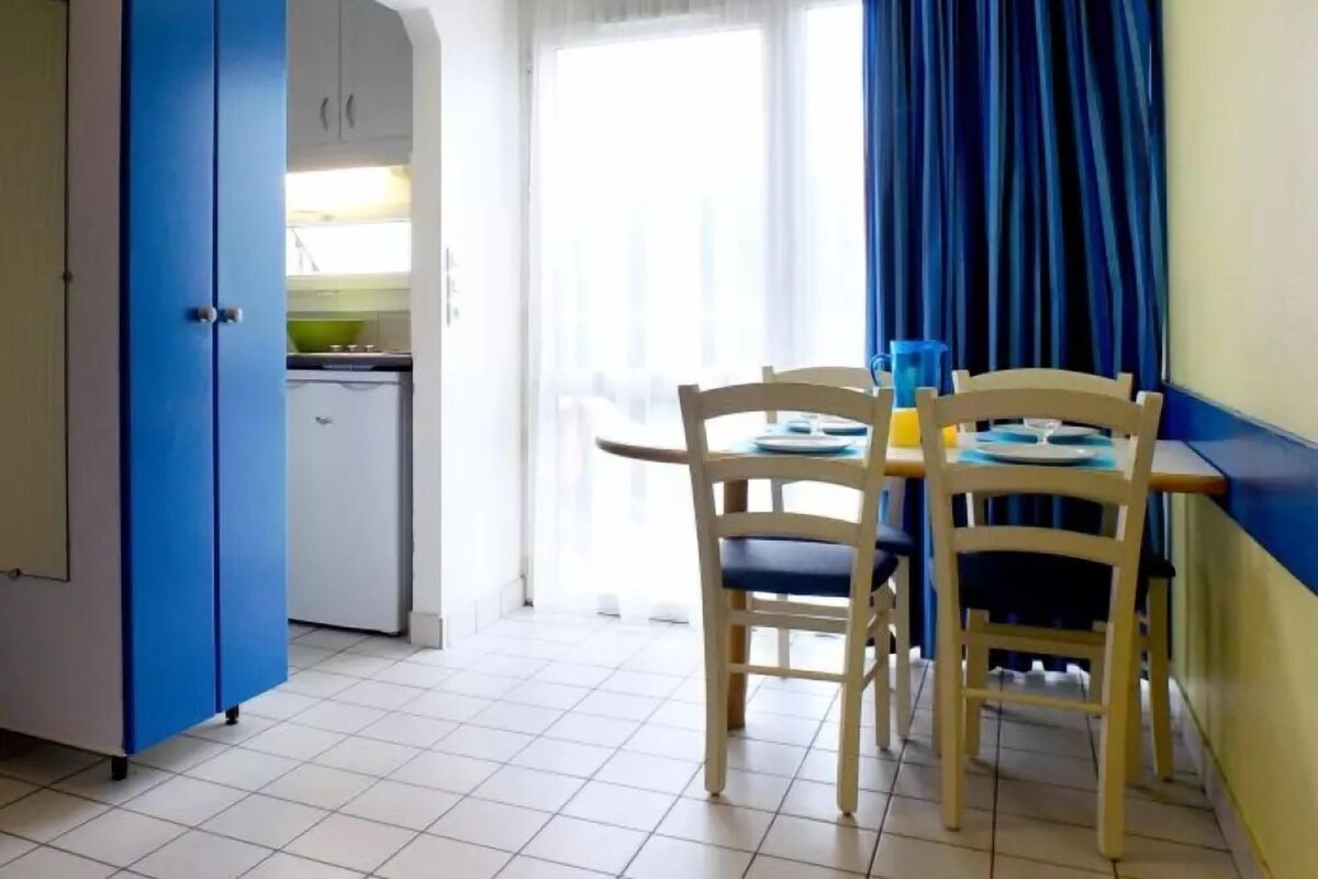 A compact kitchen with a white fridge, a blue cabinet, and a dining area with two wooden chairs and a table.