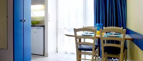 A compact kitchen with a white fridge, a blue cabinet, and a dining area with two wooden chairs and a table.
