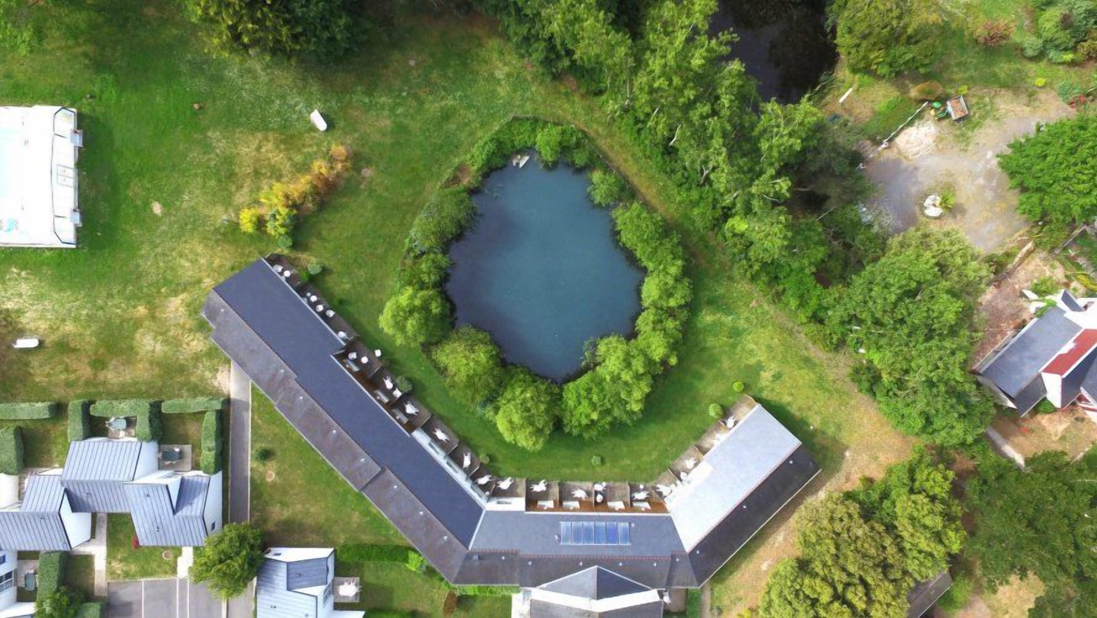 Luchtbeeld van een pand met een groot gebouw, een vijver en omliggend groen.