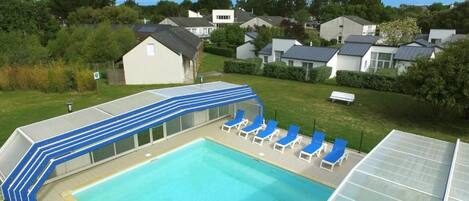 Una piscina con terraza techada y sillas de descanso.