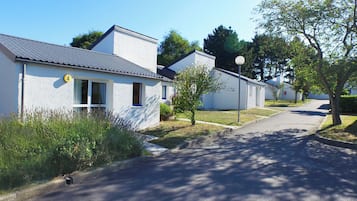 Une rangée de bâtiments blancs, avec une route pavée devant, un petit arbre et un lampadaire.