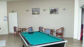 Une table de billard dans une pièce où se trouvent des chaises, un radiateur et des tableaux encadrés accrochés au mur.