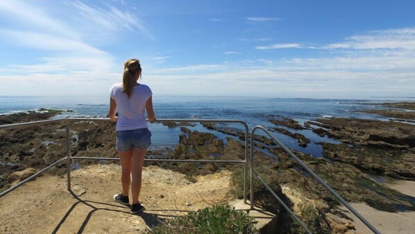 A person standing on a concrete platform overlooking a rocky shoreline with a metal railing. - Vvf Villages Piriac Sur Mer (Piriac-sur-Mer)