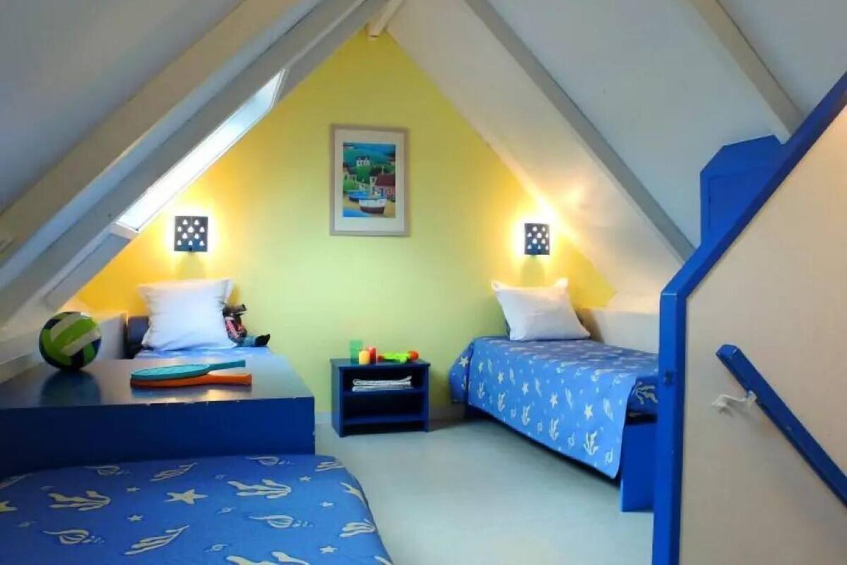 A small, triangular attic bedroom with two beds, a nightstand, and a framed picture on the wall.