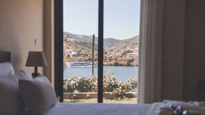 Quarto com grande janela com vista para uma colina panorâmica e um corpo d'água.
